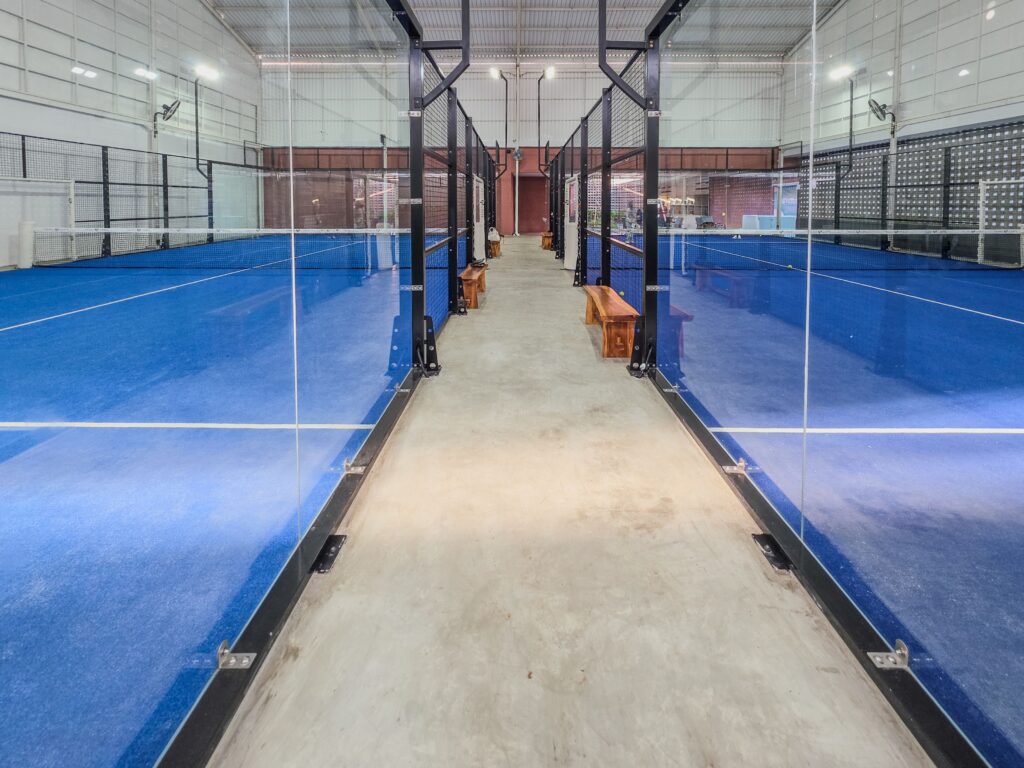Modern indoor padel tennis courts featuring bright blue surfaces and glass partitions.